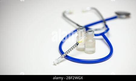 Seringue vide sur deux flacons médicaux avec stéthoscope bleu en arrière-plan. Banque D'Images