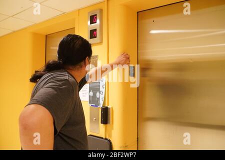 Storrs, CT / USA - 19 mars 2020: Le père asiatique penche sur le mur, attendant l'ascenseur dans les dortoirs étudiants pour arriver Banque D'Images
