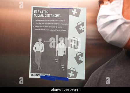 Storrs, CT / USA - 19 mars 2020: L'homme masqué penche près d'un panneau affiché dans l'ascenseur détaillant les procédures appropriées de distanciation sociale Banque D'Images