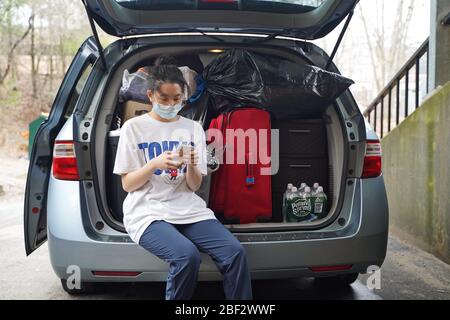 Storrs, CT / USA - 19 mars 2020: Asian girl attend ojn voiture, téléphone en main, pour sortir des dortoirs studenmt Banque D'Images