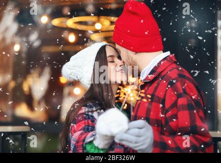 Joyeux couple avec les parciateurs de Noël à l'extérieur le jour d'hiver Banque D'Images