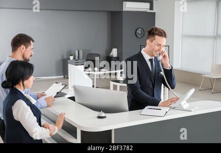 Réceptionniste masculine parlant au téléphone au bureau Banque D'Images