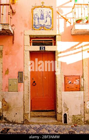 Les tuiles azulejo représentant des saints au-dessus d'une porte orange dans le quartier d'Alfama à Lisbonne Banque D'Images