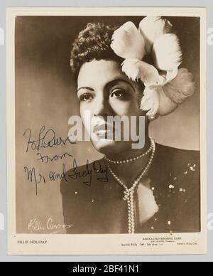Photo de Billie Holiday. Imprimé gélatine argentée représentant une image noir et blanc de Billie Holiday. Les fêtes sont représentées derrière un support de microphone. Elle porte un chemisier blanc, une ceinture et une jupe fleurie. Un groupe est représenté dans l'arrière-plan derrière elle, sur le côté gauche de l'image. Banque D'Images