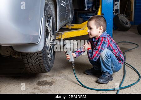 Un jeune garçon, un jeune travailleur automobile, fait un changement de pneu avec une clé pneumatique dans le garage d'une station de service. Un enfant apprend la changine mécanique Banque D'Images