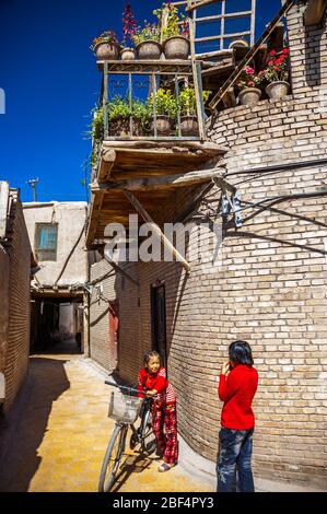 Deux jeunes filles ouïgoures dans une ruelle dans la vieille ville de la plate-forme. Ci-dessus est un balcon et jardin suspendu. Kashgar, Xinjiang Banque D'Images