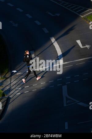 17 avril 2020, Hessen, Francfort-sur-le-Main: Entre les rangées de maisons dans le centre-ville, le soleil du matin crée une bande de lumière sur une rue qui est traversé par un jogger. Photo: Arne Dedert/dpa Banque D'Images