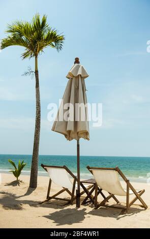Deux chaises longues parapluie et cococotier face à la mer sur la plage idyllique Banque D'Images