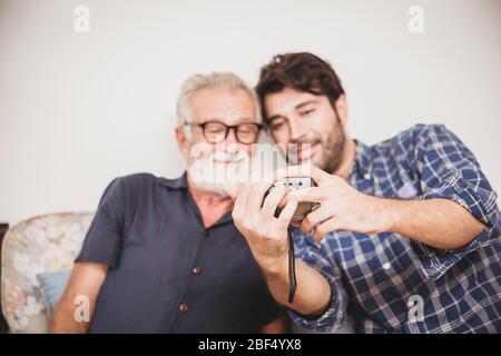 Un aîné regardant rejouer des photos de l'appareil photo numérique avec son fils bonheur famille moment avec le concept de dispositif numérique. Banque D'Images