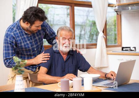 Soins aux aînés à domicile, bon mentor sain vieil homme intelligent utilisant ordinateur portable séjour chez le jeune homme. Banque D'Images