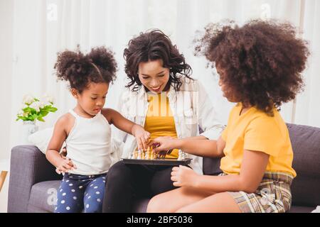 Smart mère bon soin, enseignant à ses enfants d'être génie et astucieux petites filles apprendre à jouer le jeu d'échecs en vacances à la maison. Banque D'Images