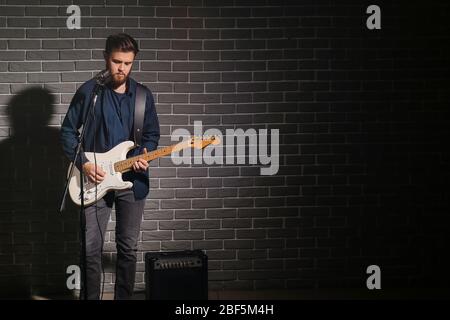 Jeune homme jouant de la guitare près du mur de briques sombres Banque D'Images