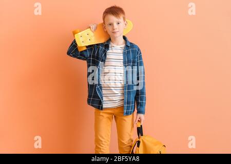 Joli petit garçon avec skate et sac à dos sur fond couleur Banque D'Images