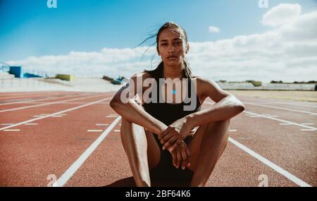 Athlète femme assis sur la piste et le stade de terrain. Coureur se reposant sur la piste de course après la séance de formation. Banque D'Images