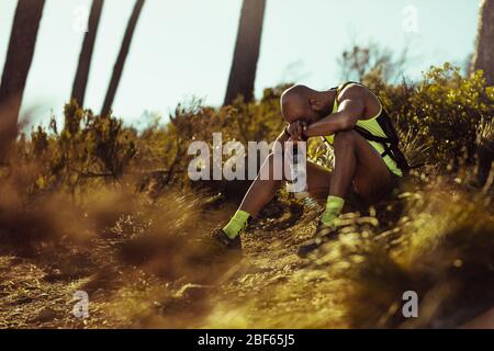 Homme dans des vêtements de sport assis sur le groupe et se détendre après l'entraînement de course de sentier. Coureur de piste masculin se brisant après un entraînement de course sur un sentier de montagne. Banque D'Images