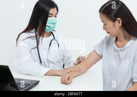 Une jeune femme médecin asiatique portant un masque médical et un stéthoscope examine la patiente et la traite en injectant des médicaments dans une clinique ou un hôpital. h Banque D'Images