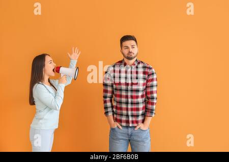 Une femme en colère avec une mégaphone criant à son mari sur fond de couleur Banque D'Images