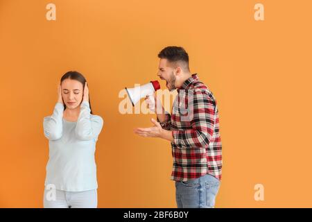 Homme en colère avec mégaphone criant à sa femme sur fond de couleur Banque D'Images