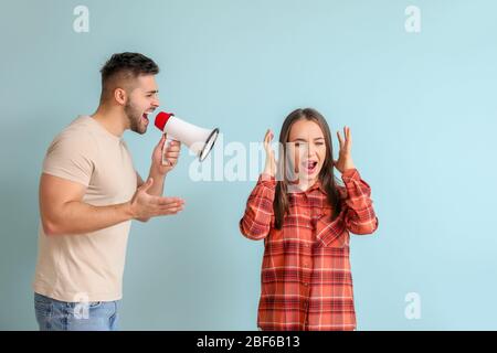 Homme en colère avec mégaphone criant à sa femme sur fond de couleur Banque D'Images