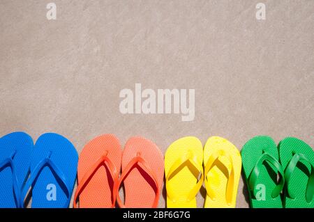 Groupe de tongs dans des couleurs vives d'été alignées sur la plage de sable lisse Banque D'Images