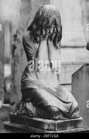 sculpture noire et blanche d'une fille d'ange dans un vieux cimetière. Gros plan d'ange lapié avec des yeux fermés et monument croisé au cimetière. Cimetière vieux W Banque D'Images