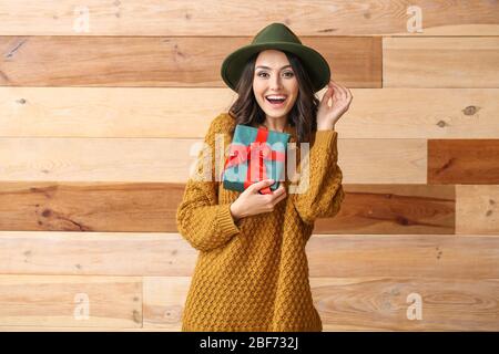 Belle jeune femme en sweat chaud et avec cadeau sur fond en bois Banque D'Images