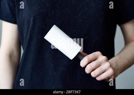 Une femme non reconnaissable nettoie un t-shirt noir avec un rouleau de vêtements. Banque D'Images