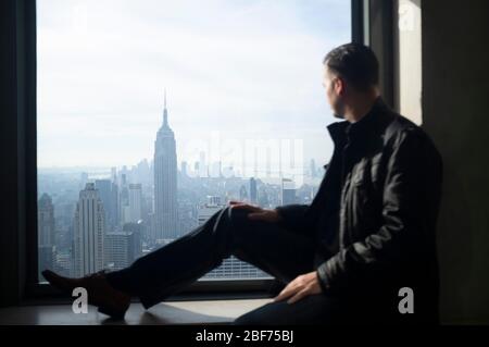 Homme regardant la fenêtre. L'Empire State Building et Manhattan à l'extérieur, une journée très ensoleillée. Banque D'Images