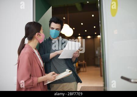 Un jeune couple professionnel porte des masques de protection debout au bureau et s'est parlé les uns avec les autres Banque D'Images