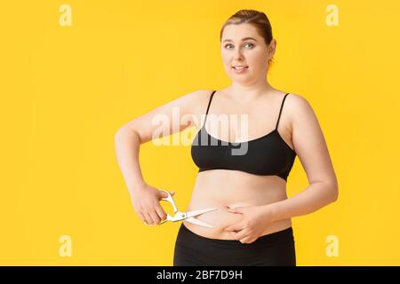 Femme en surpoids avec ciseaux sur fond couleur. Concept de perte de poids Banque D'Images