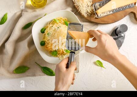 Femme gravant du fromage sur la plaque avec de délicieuses pâtes, vue de dessus Banque D'Images