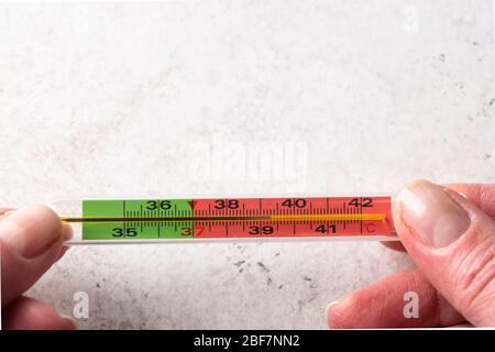 Les mains de la femme tiennent le thermomètre au mercure sur fond blanc. Fièvre et concept de santé. Vue de dessus Banque D'Images