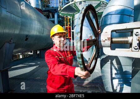 Aktobe Region/Kazakhstan - 04 mai 2012: Usine de raffinerie de pétrole. Employé de maintenance en cas d'usure de travail rouge et de casque jaune qui règle la direction technologique wh Banque D'Images