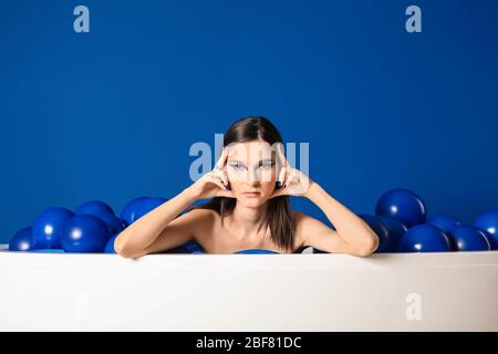 Portrait de la jeune femme à la mode avec des ballons d'air assis dans la baignoire sur fond bleu Banque D'Images