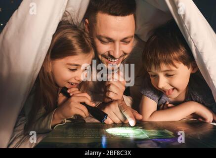 Père et ses petits enfants lisant l'histoire du coucher à la maison Banque D'Images