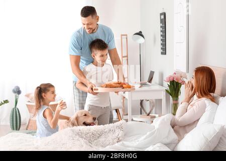 Un mari heureux avec des enfants qui apportent son petit déjeuner à la femme au lit Banque D'Images