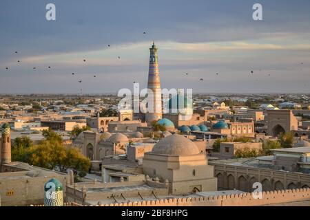 Magnifique paysage urbain avec grand minaret islamique sur Khiva, Ouzbékistan, vu de l'air au coucher du soleil, avec des oiseaux dans le ciel. Belle architecture patrimoniale Banque D'Images