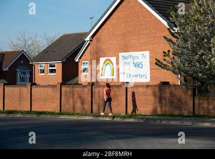 Lady Runner marchant devant un NHS et KeyWorkers merci bannière. Aussi avec un arc-en-ciel peint sur la maison, dans le cadre du blocage du coronavirus au Royaume-Uni Banque D'Images