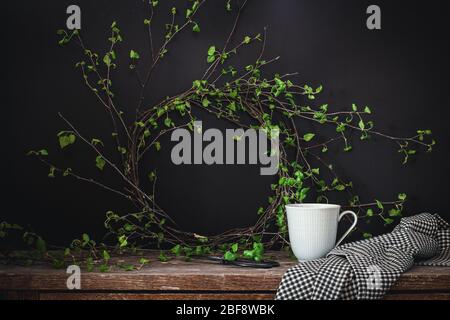 Couronne de printemps faite de jeunes branches de bouleau et une tasse de thé sur fond sombre Banque D'Images