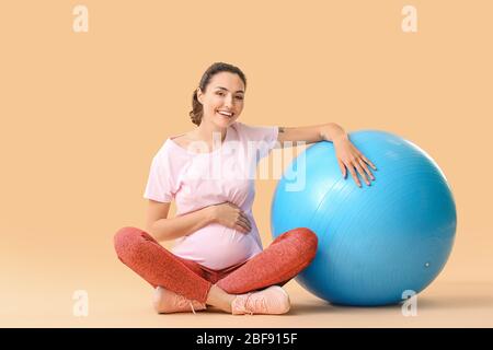 Jeune femme enceinte faisant des exercices avec le fitball sur fond de couleur Banque D'Images