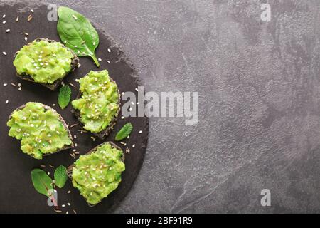 Plaque en ardoise avec de délicieux sandwichs avocat sur fond sombre Banque D'Images