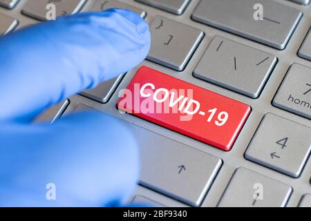 Concept de coronavirus. Clavier avec touche rouge et message COVID-19. Un doigt bleu ganté appuie sur un bouton. Banque D'Images