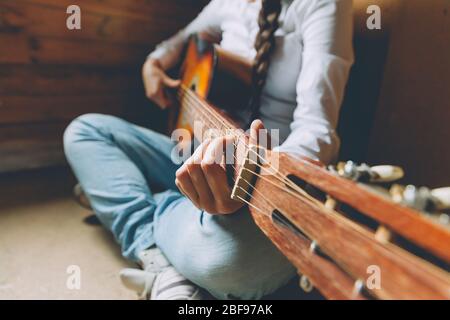 Restez à la maison en toute sécurité. Jeune femme assise à la maison et jouant de la guitare, les mains se rapprochant. Jeune fille apprenant à jouer la chanson et à écrire de la musique. Loisirs style de vie détente instrument loisirs éducation concept Banque D'Images