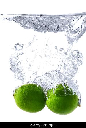 Chute de limes fraîches dans l'eau sur fond blanc Banque D'Images