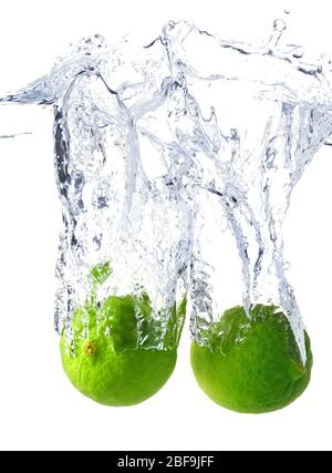 Chute de limes fraîches dans l'eau sur fond blanc Banque D'Images