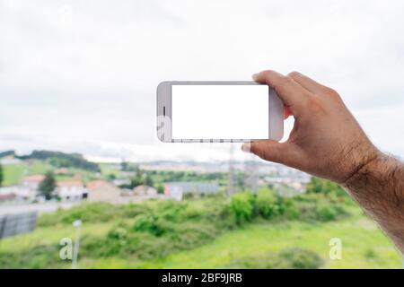 Gros plan une main tient un téléphone mobile pour prendre une photo de la fenêtre d'une maison Banque D'Images