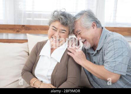 Romantique et heureux asiatique, couple senior riant tout en s'asseyant sur un canapé à la maison Banque D'Images