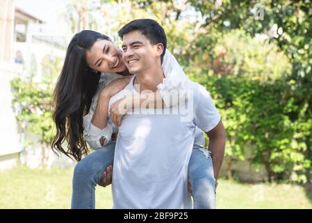 Portrait de l'adorable gars caucasien romantique en chemise à carreaux, la dame asiatique rêveuse le conduit à l'arrière. Loisirs, bonheur de détente, promenade sur gazon, détente, romance Banque D'Images