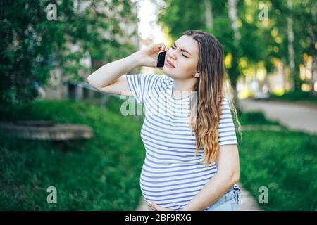 Femme enceinte avec contractions sensation douleur appelant ambulance avec téléphone cellulaire dans le parc Banque D'Images