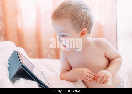 Portrait d'un petit garçon qui regarde une drôle de dessin animé sur un comprimé et rires. Un enfant joue sur la tablette à la maison et souriant. Banque D'Images